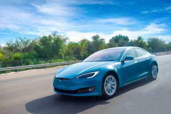 A blue coloured electric car cruising on highway,with clear blue sky.green energy concept.Have space for text.
